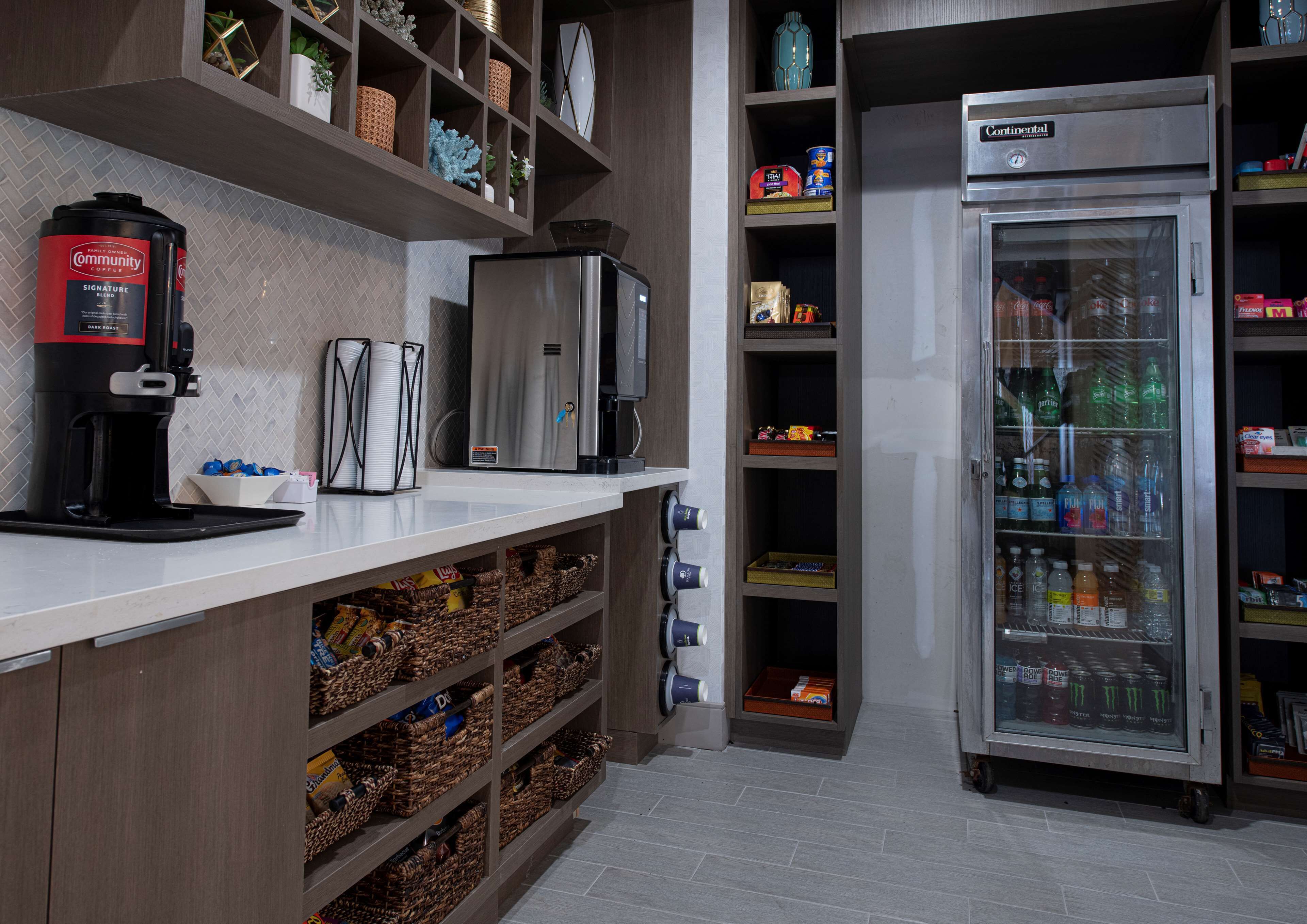 Una kitchenette con cafetera, refrigerador y estantes con diversos objetos.