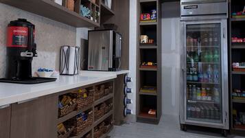 Una kitchenette con cafetera, refrigerador y estantes con diversos objetos.