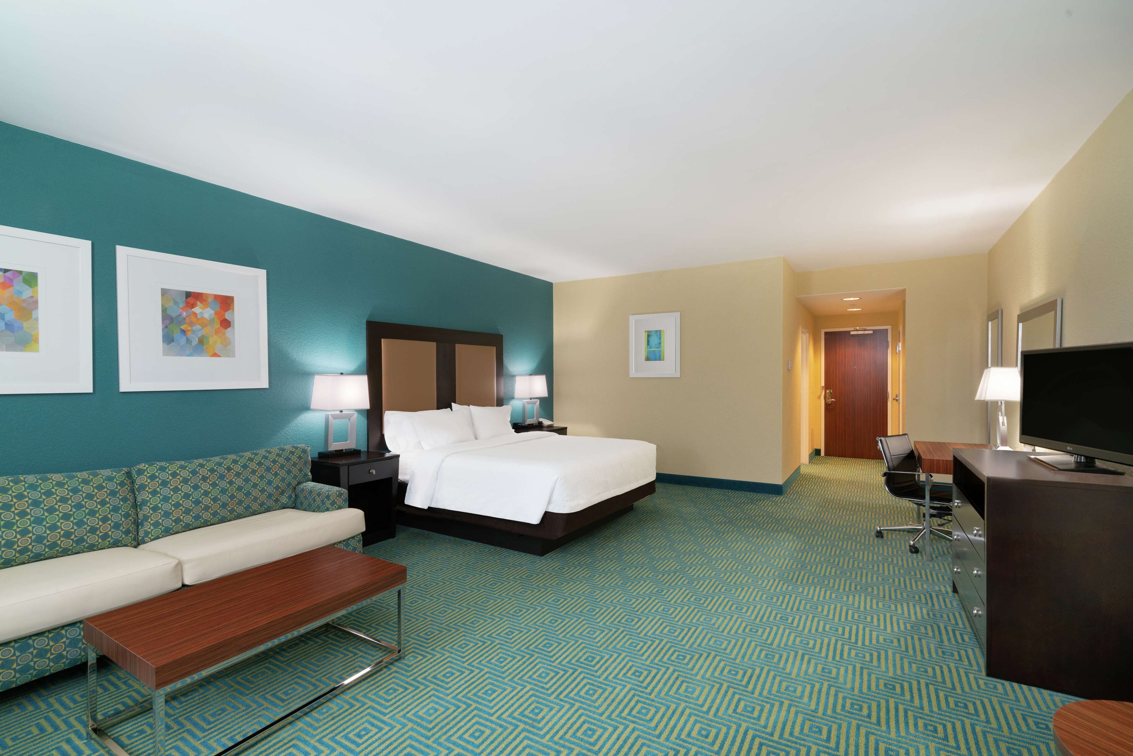 A hotel room with a bed, a sofa, a desk, and a TV.