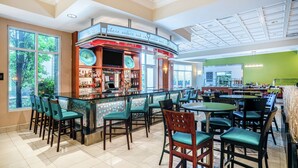 Un restaurant doté d'un bar, de chaises vertes et offrant une vue sur les arbres à travers de grandes fenêtres.