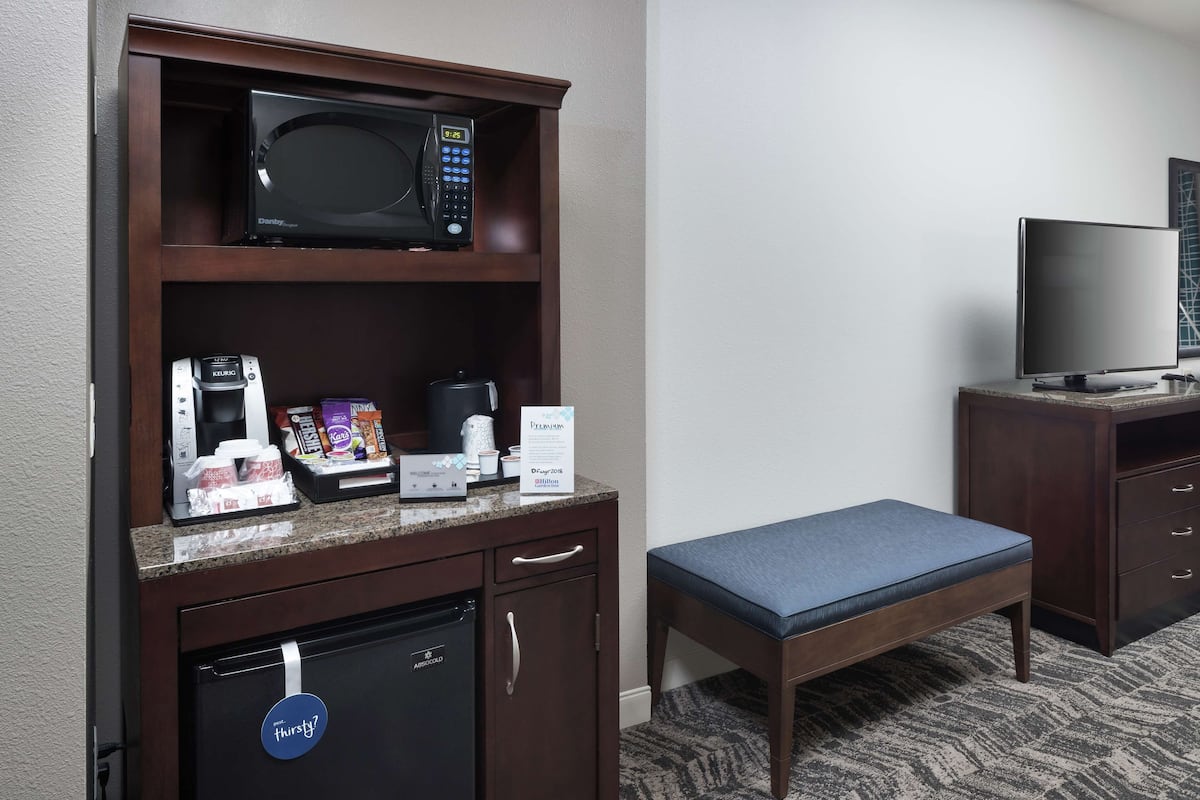 A kitchenette with a microwave, coffee maker, and refrigerator. There is a small table with a cushion and a television on a stand.