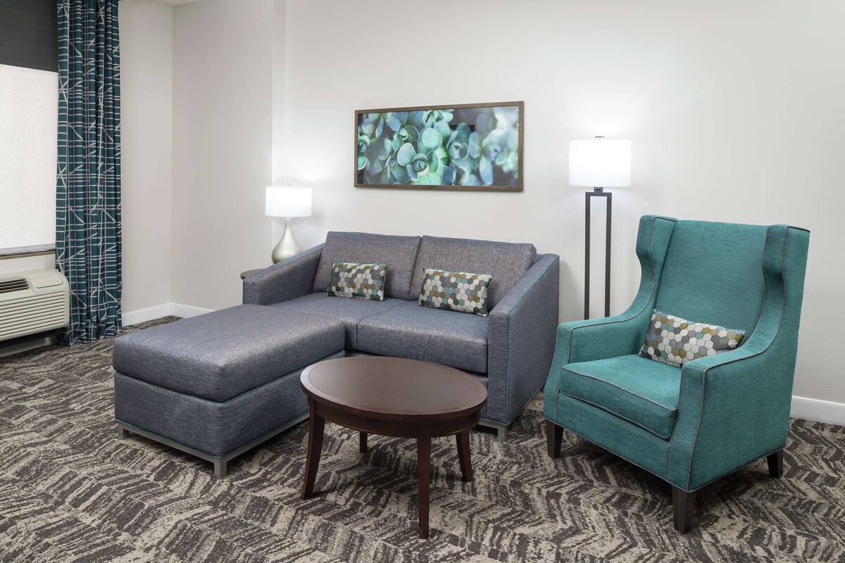 A living room with a grey sectional sofa, a teal armchair, a round coffee table, and a floor lamp.