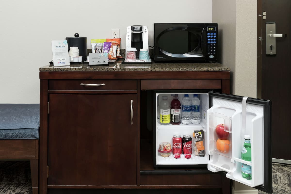 A compact kitchenette with a microwave, coffee maker, and a refrigerator stocked with beverages and snacks.