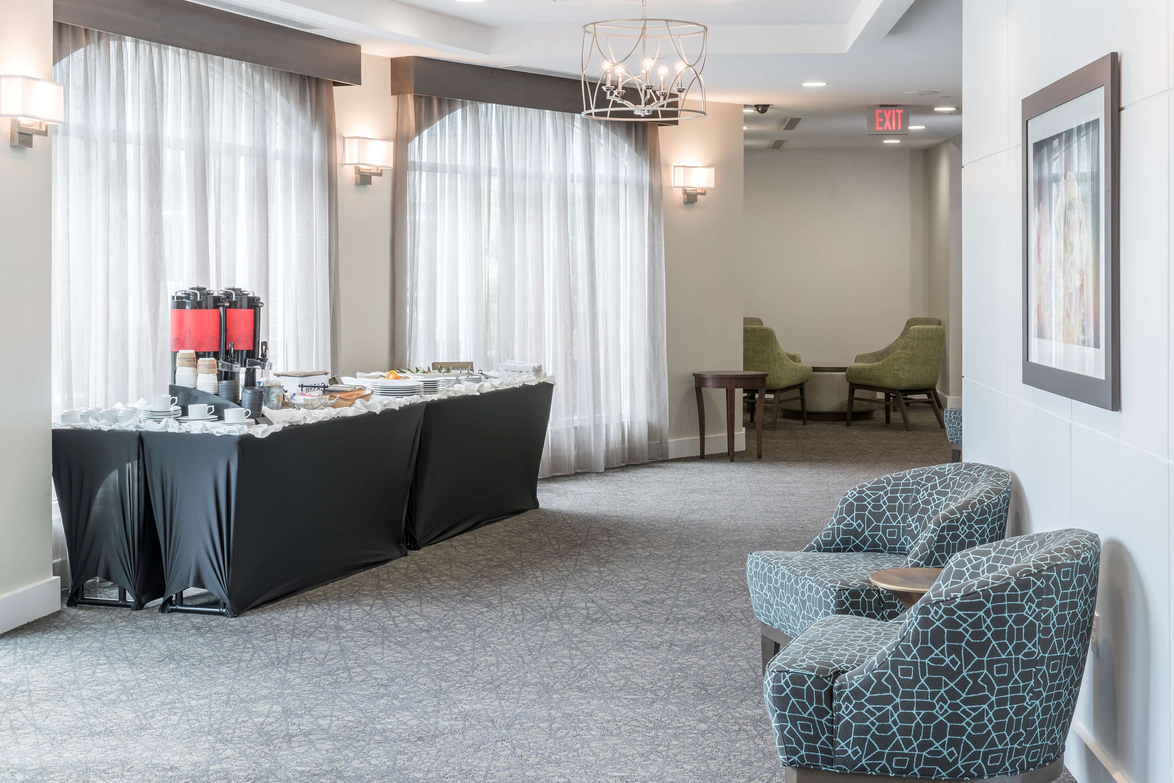 A hotel lobby with a reception desk, a chandelier, a seating area with two chairs, and a framed picture on the wall.