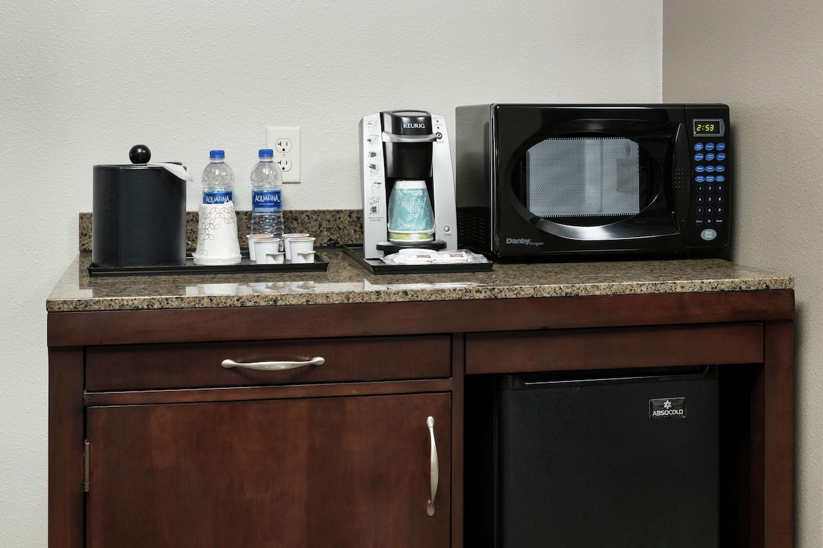 A kitchenette with a coffee maker, microwave, and water bottles on the counter.