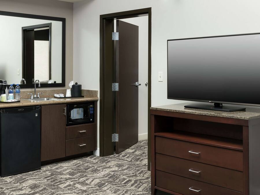 Ein Hotelzimmer mit Küchenzeile, einem Flachbildfernseher, einem großen Spiegel und Teppichboden.
