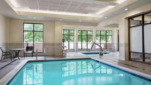 An indoor swimming pool with clear glass walls, a tiled floor, and a ceiling with recessed lighting. - Hilton Garden Inn Charlotte/Ayrsley (Charlotte)