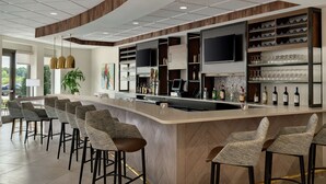 A modern bar area with a curved counter, multiple seating options, and a variety of bar tools and glassware. - Hilton Garden Inn Charlotte/Ayrsley (Charlotte)