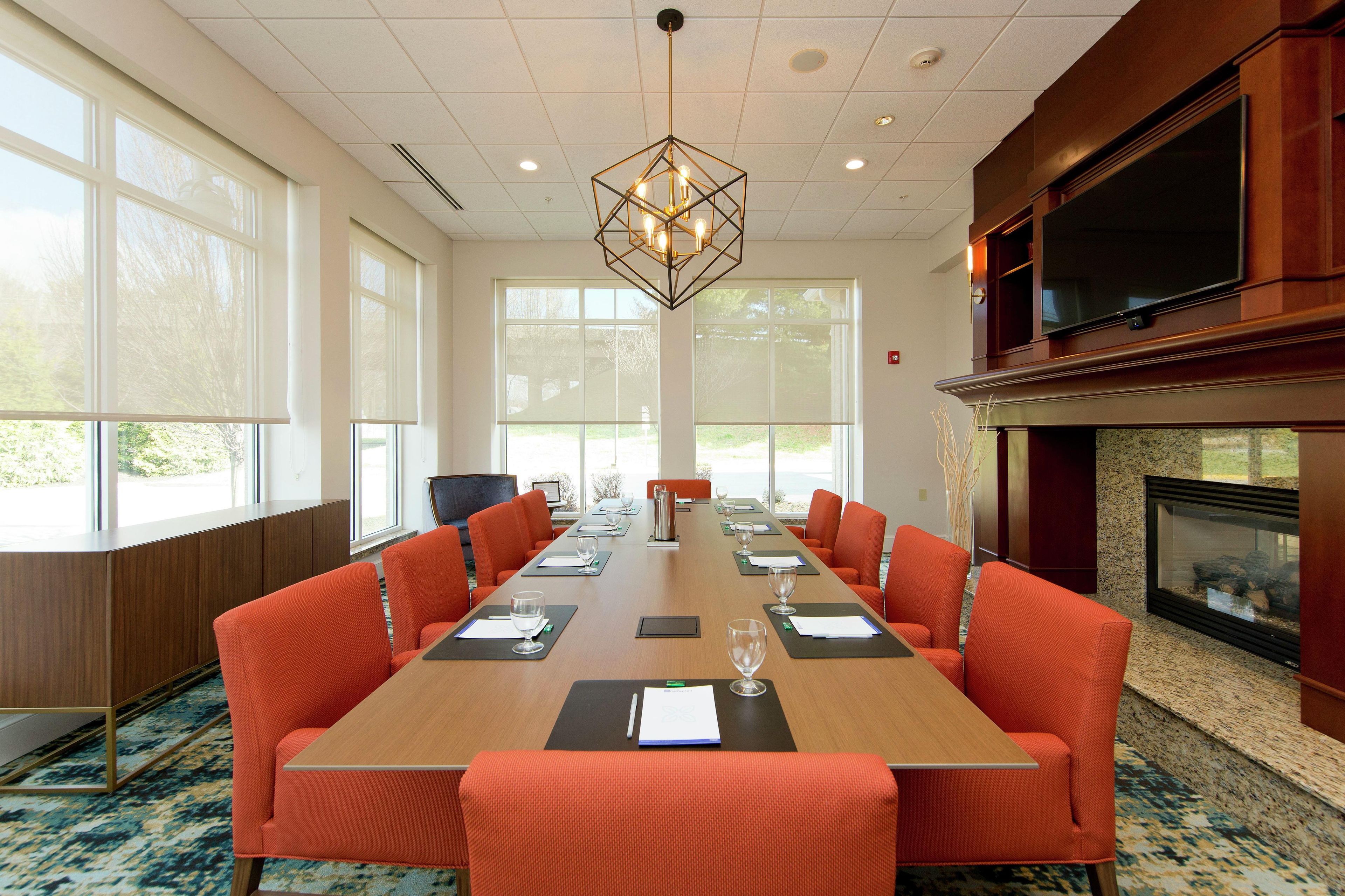 A conference room with a long table, orange chairs, and a fireplace.