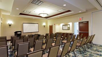 A conference room with rows of chairs, a projector screen, and an exit door.