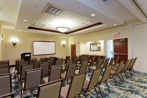 A conference room with rows of chairs, a projector screen, and an exit door. - Hilton Garden Inn Winchester (Winchester)