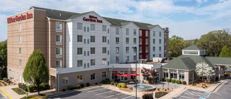 Un Hilton Garden Inn con estacionamiento, una fuente y un pequeño jardín.