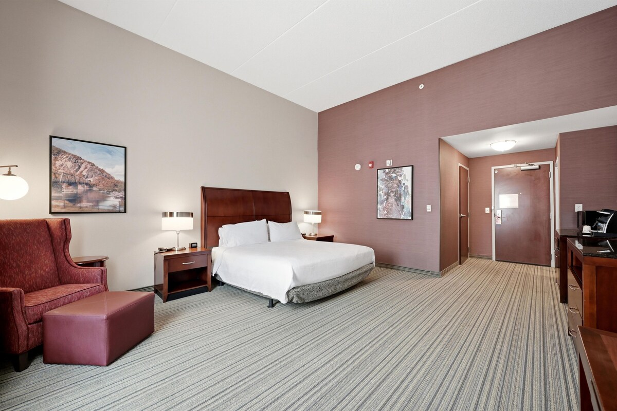 A hotel room with a bed, a chair, a desk, a lamp, and a picture on the wall.