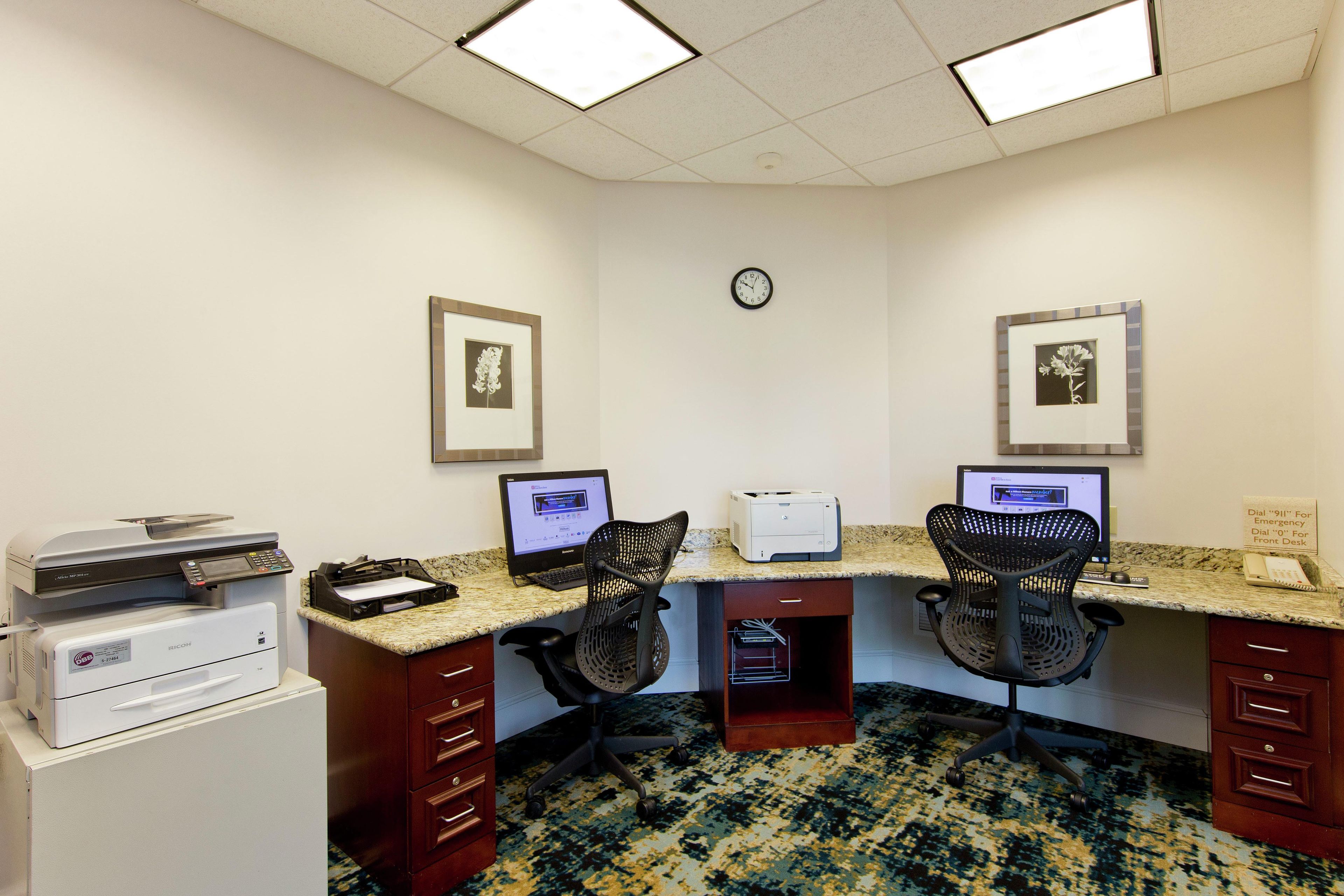 A workspace with two desks, computers, printers, and chairs.
