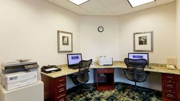 A workspace with two desks, computers, printers, and chairs.