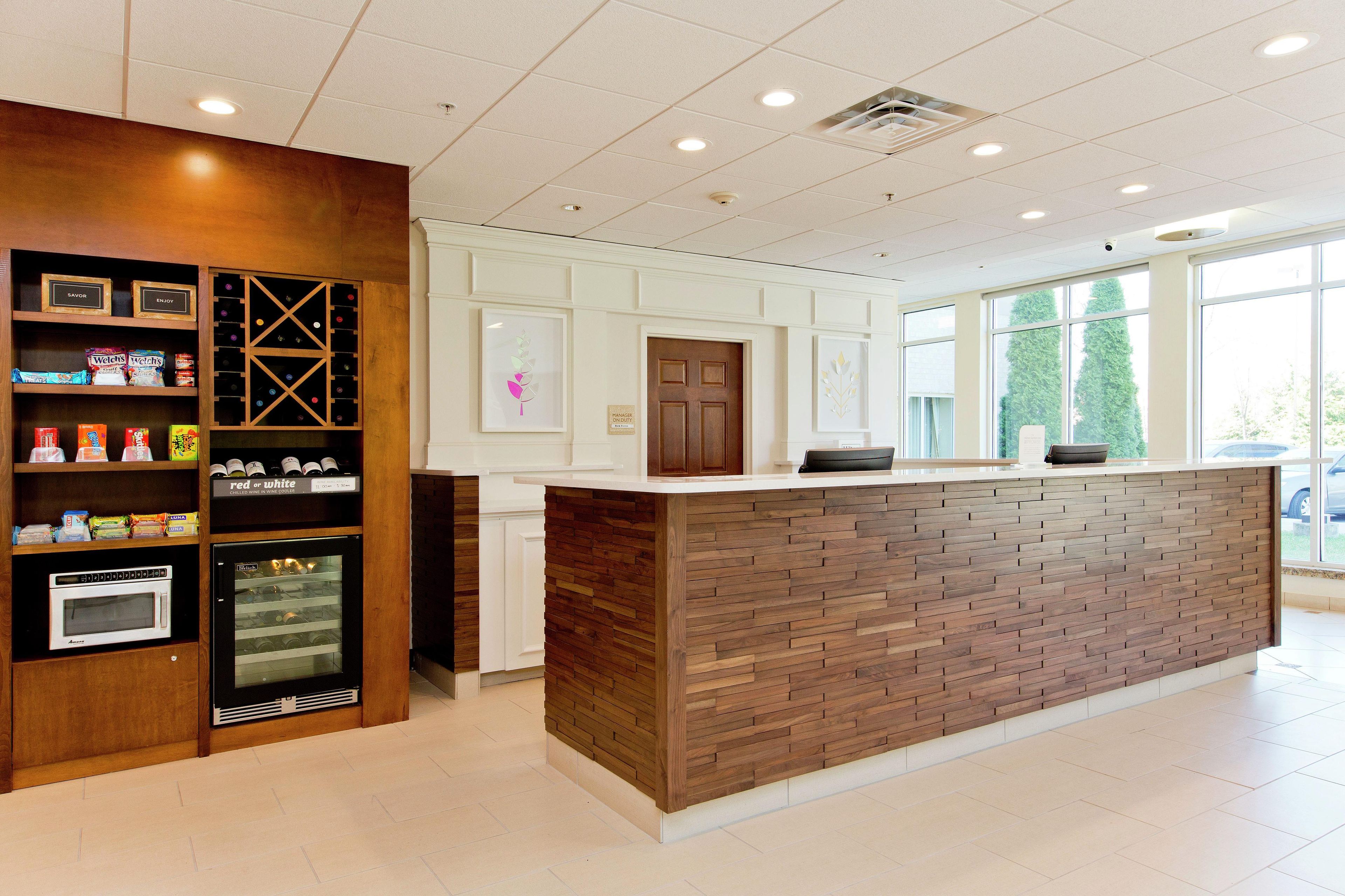 A reception area with a wooden reception desk, a wine cooler, and shelves with snacks and beverages.