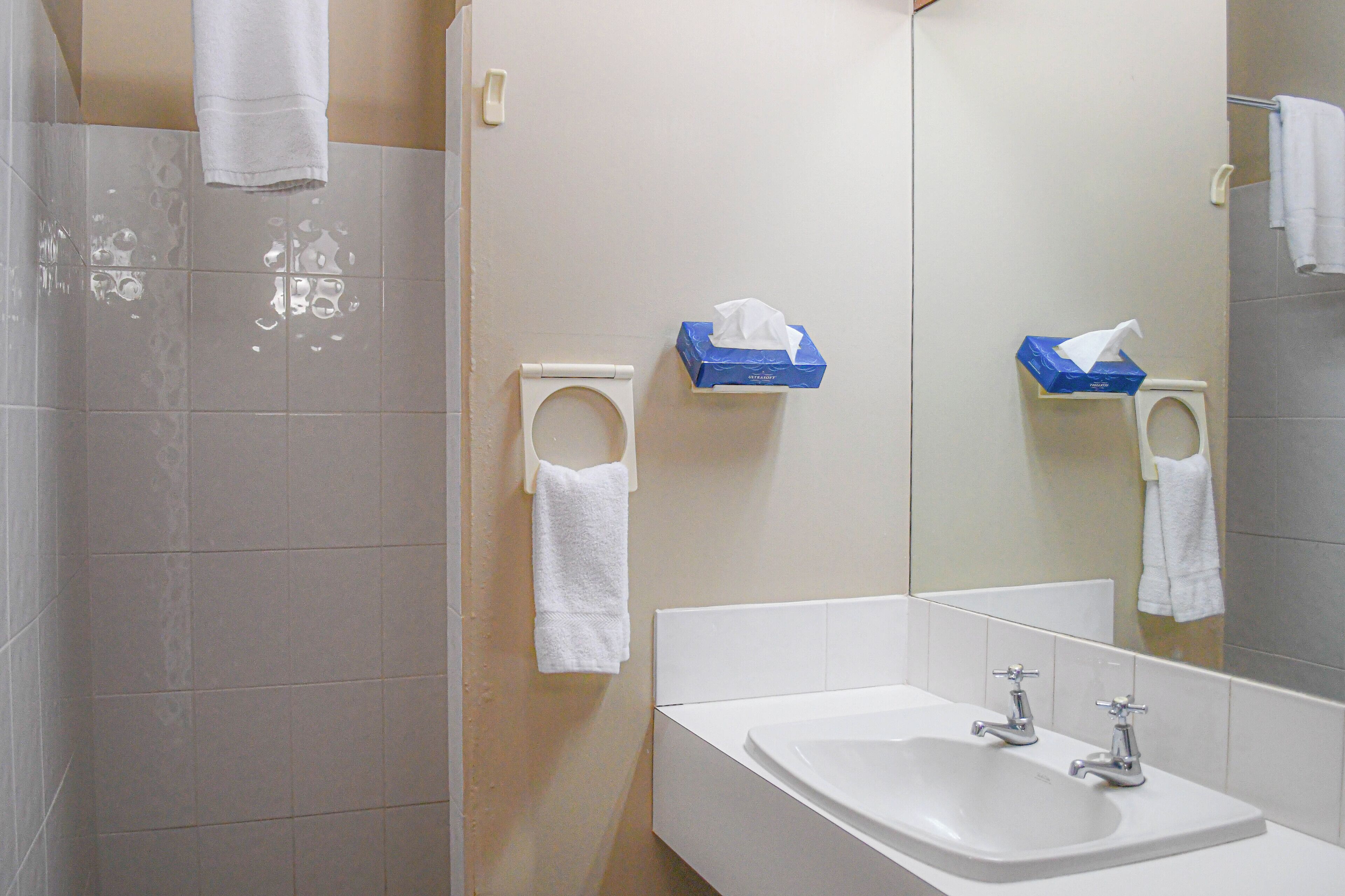 A bathroom with a sink, two faucets, a mirror, and a towel rack with a white towel.