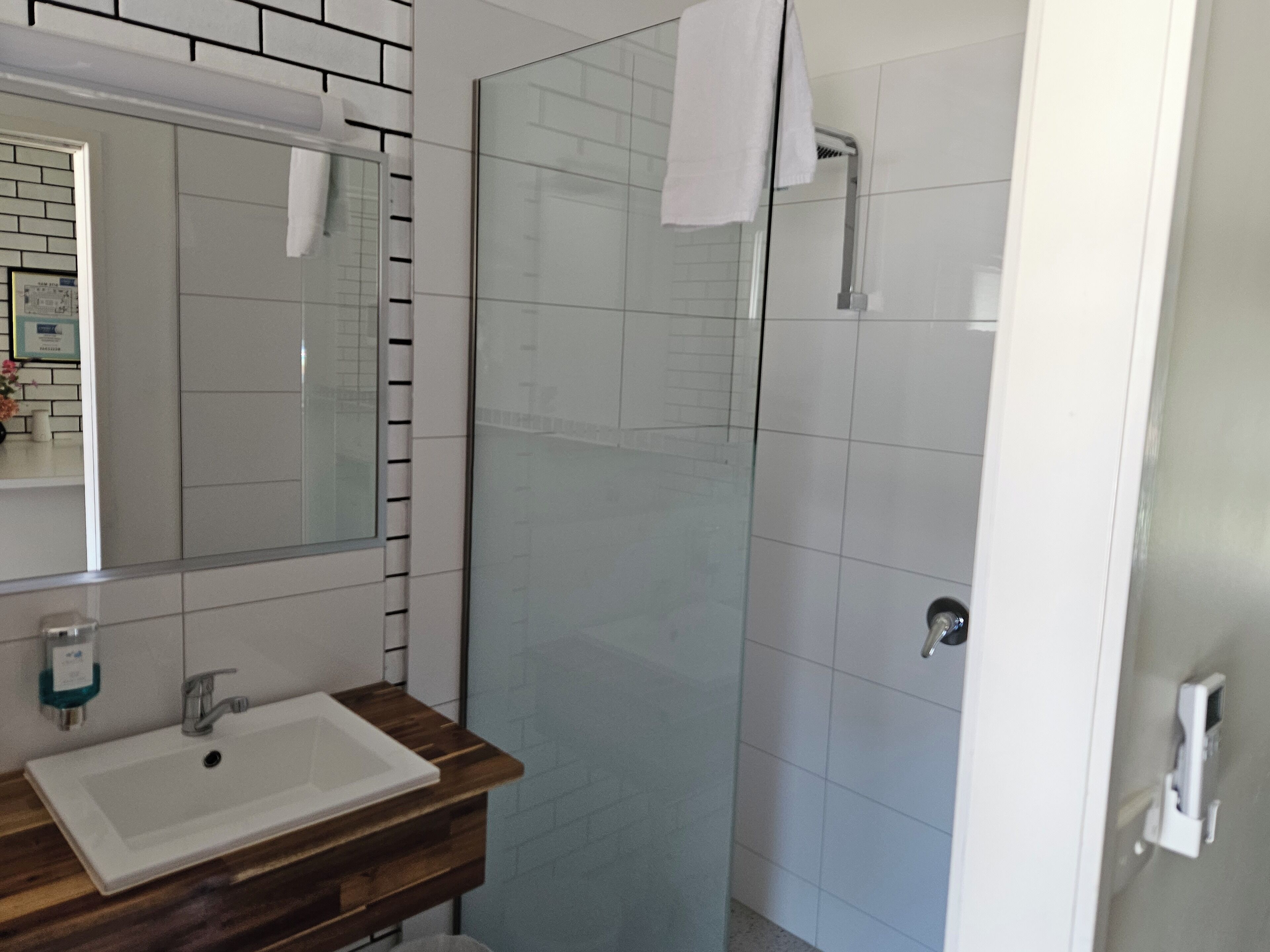 Un baño con tocador de madera, un lavabo blanco, cabina de ducha de vidrio y piso de baldosas.