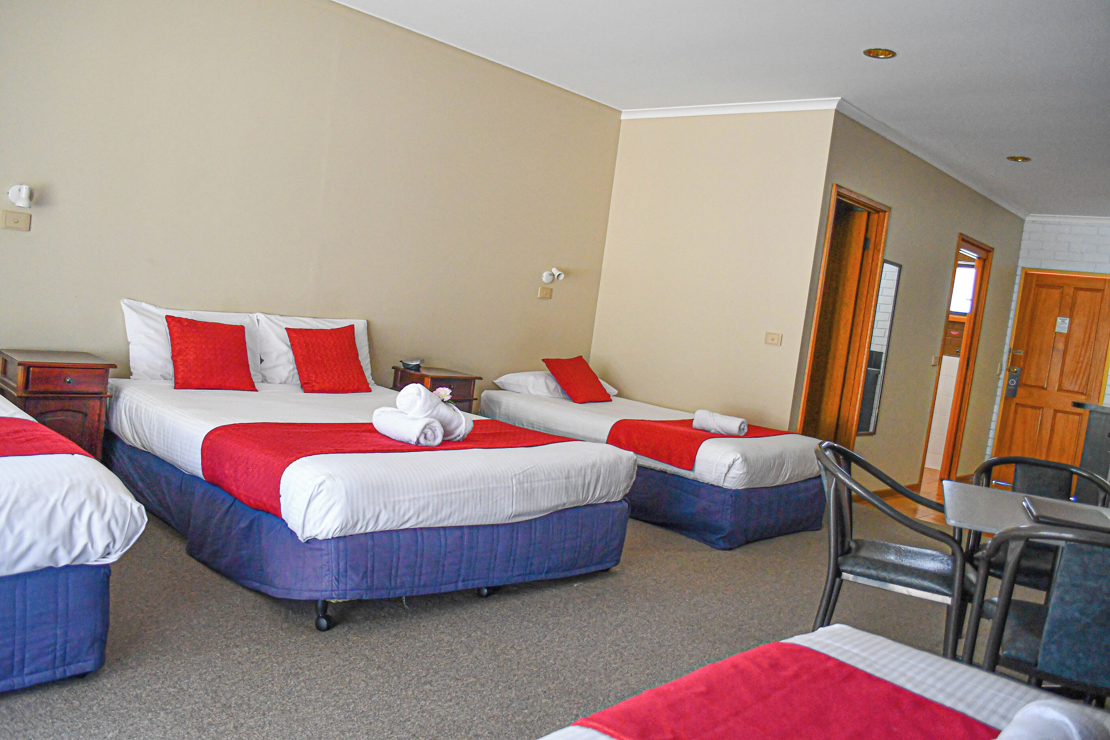 Une chambre d’h ôtel avec trois lits, chacun recouvert d’une literie rouge et blanche, et une petite table avec des chaises.