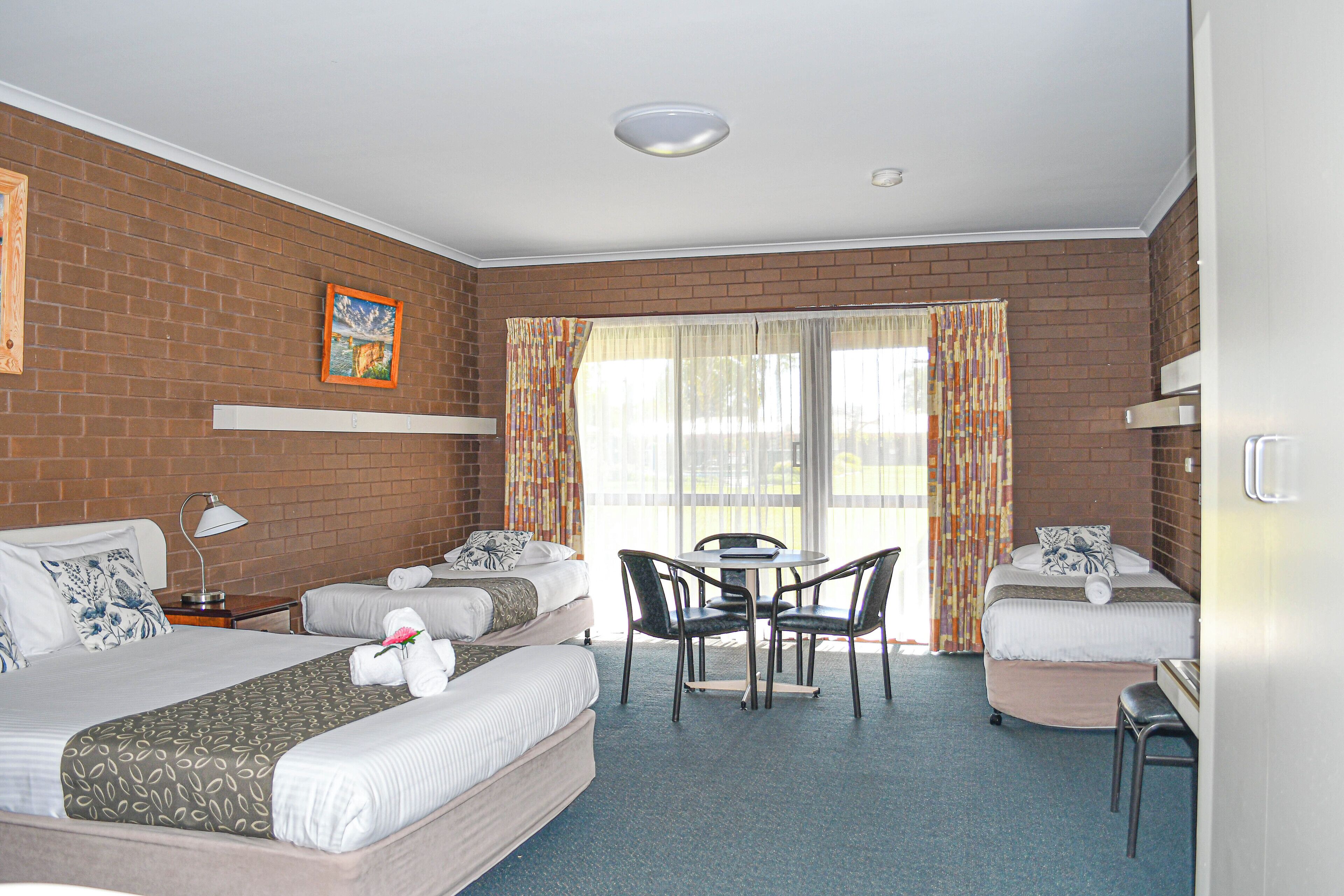 A hotel room with two beds, a dining table, and a small desk.