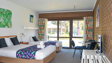 A hotel room with two beds, a desk, and a chair. There is a window with curtains and a view of the outside.