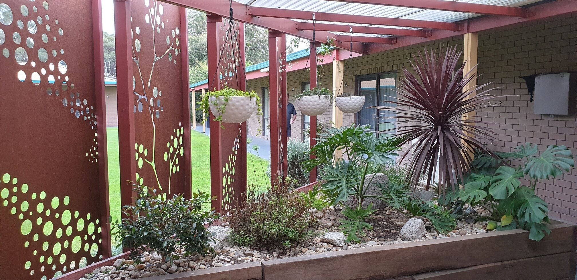 Un espace jardin aménagé et abrité, avec une clôture en métal rouge, des jardinières suspendues et diverses plantes.