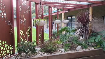 Un espace jardin aménagé et abrité, avec une clôture en métal rouge, des jardinières suspendues et diverses plantes.