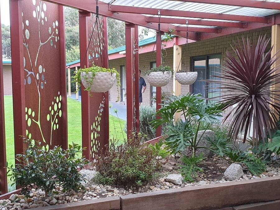 Un espace jardin aménagé et abrité, avec une clôture en métal rouge, des jardinières suspendues et diverses plantes.