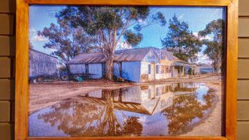 A framed painting of a rural scene with houses and trees reflected in a puddle.