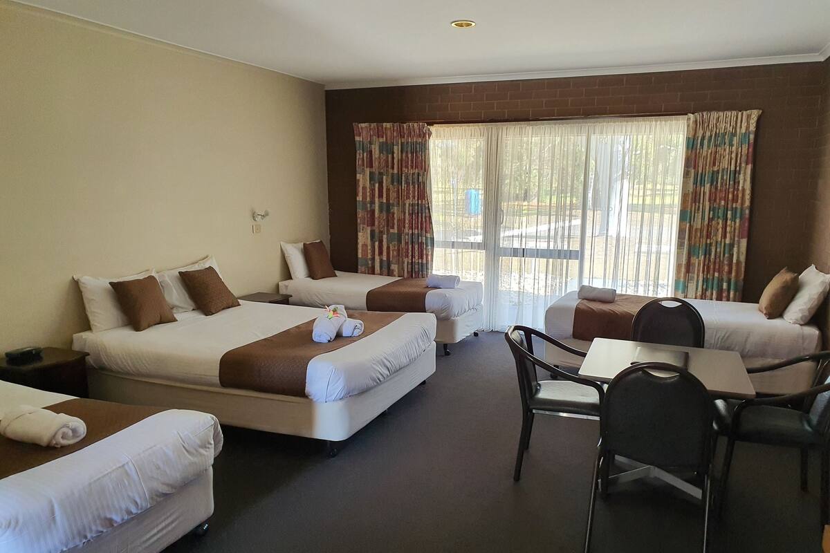 A hotel room with two single beds, a double bed, a desk, and a chair.