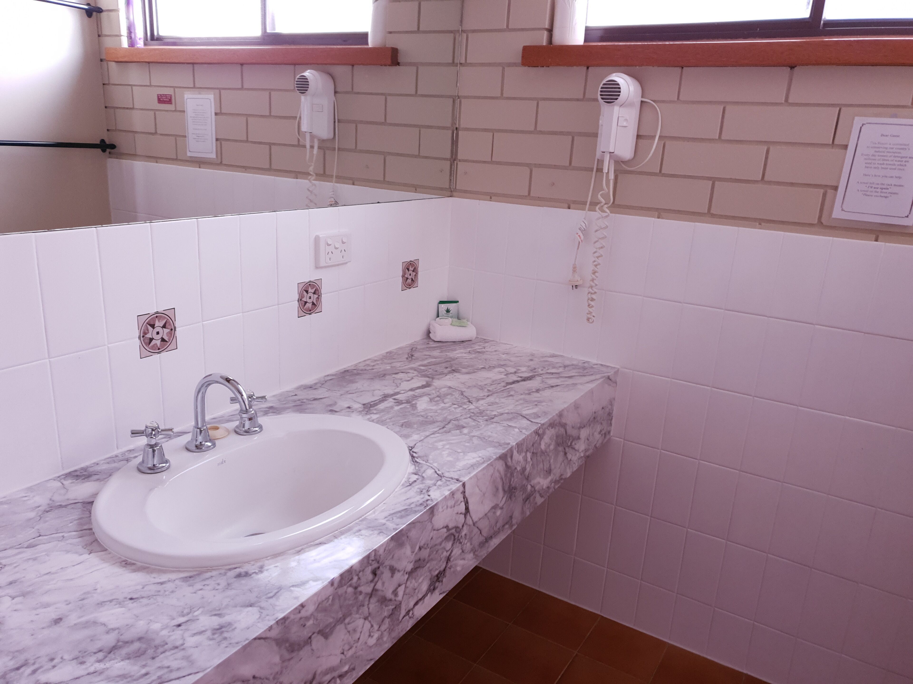 Een badkamer met een marmeren wastafel, een spiegel en twee haardroger apparaten bevestigd aan de muur.