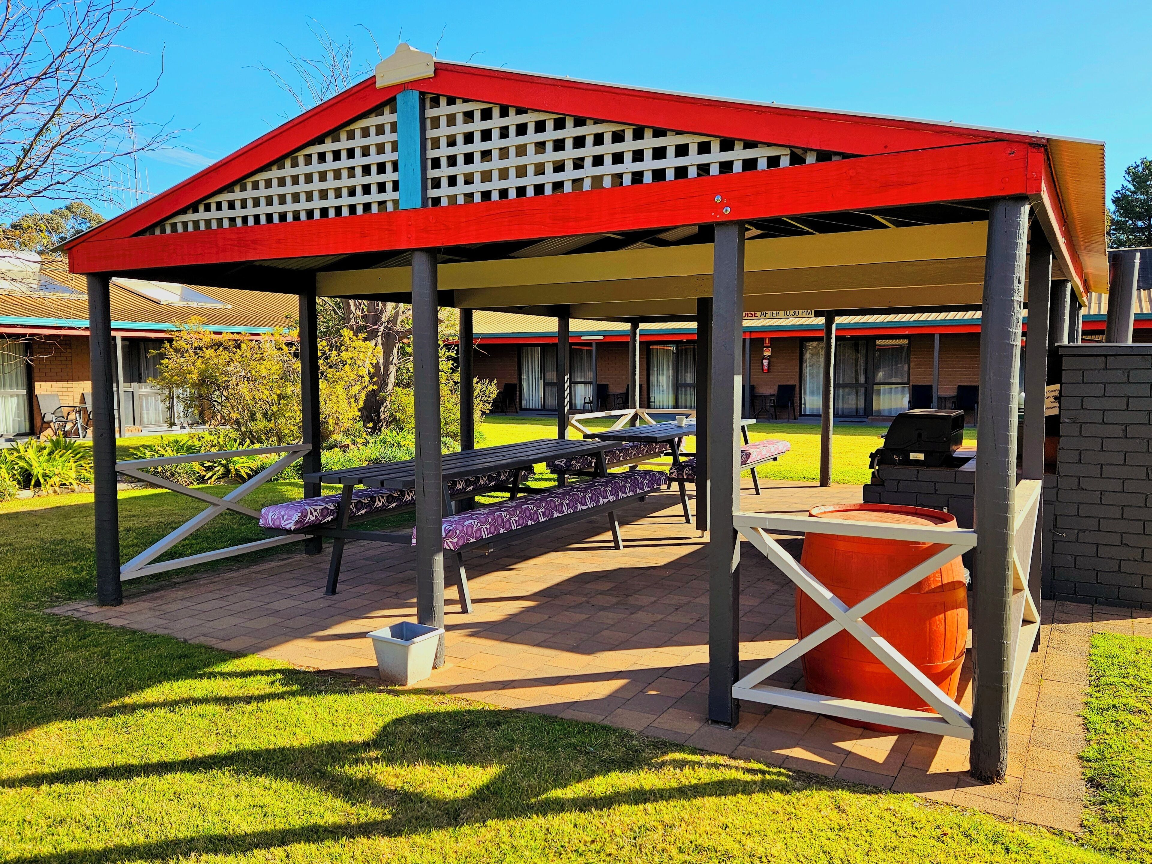 A covered outdoor seating area with picnic tables and a barbecue grill.