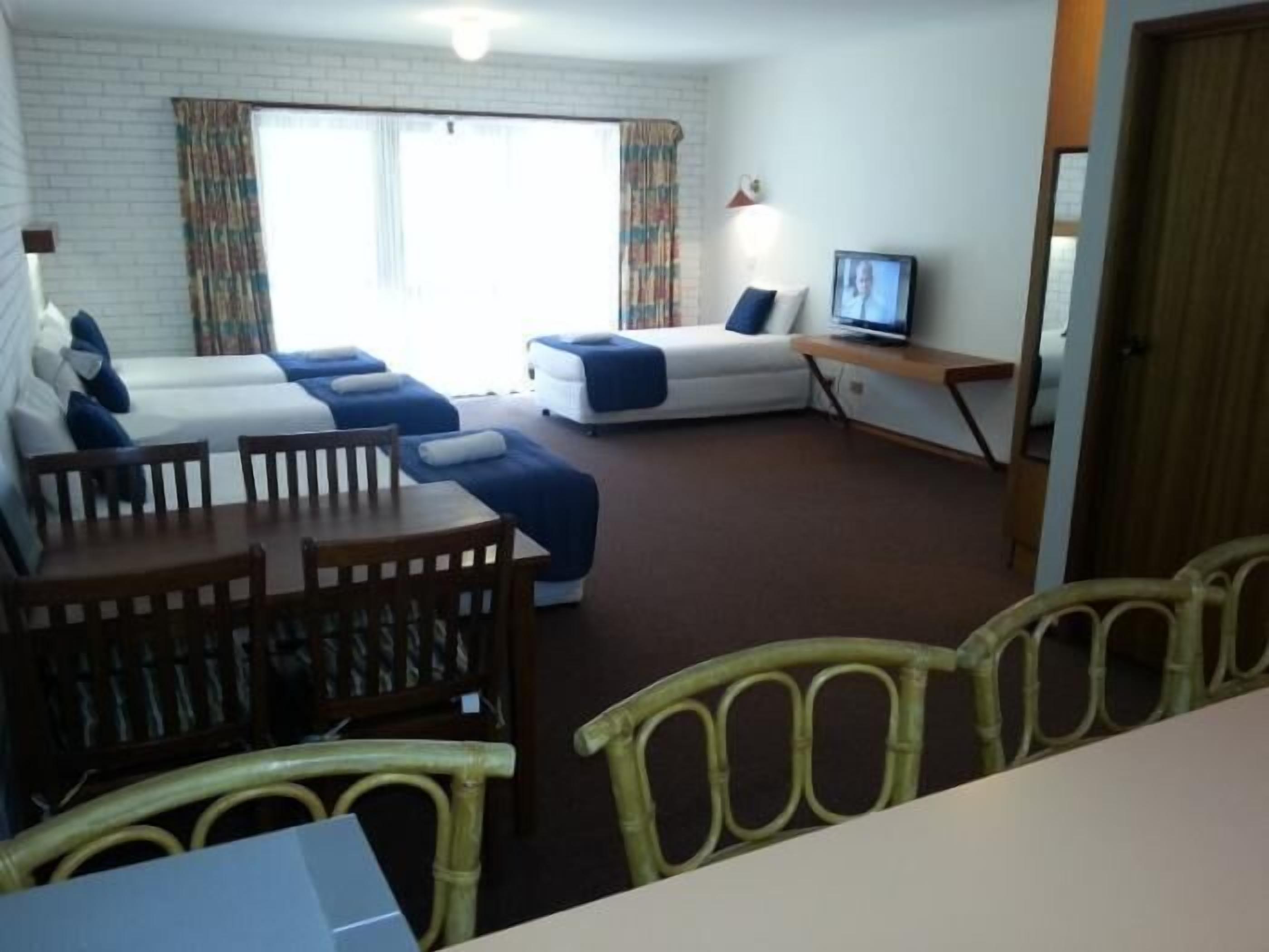 Une chambre d’hôtel avec deux lits simples, une télévision, une table à manger avec des chaises et une fenêtre avec des rideaux.