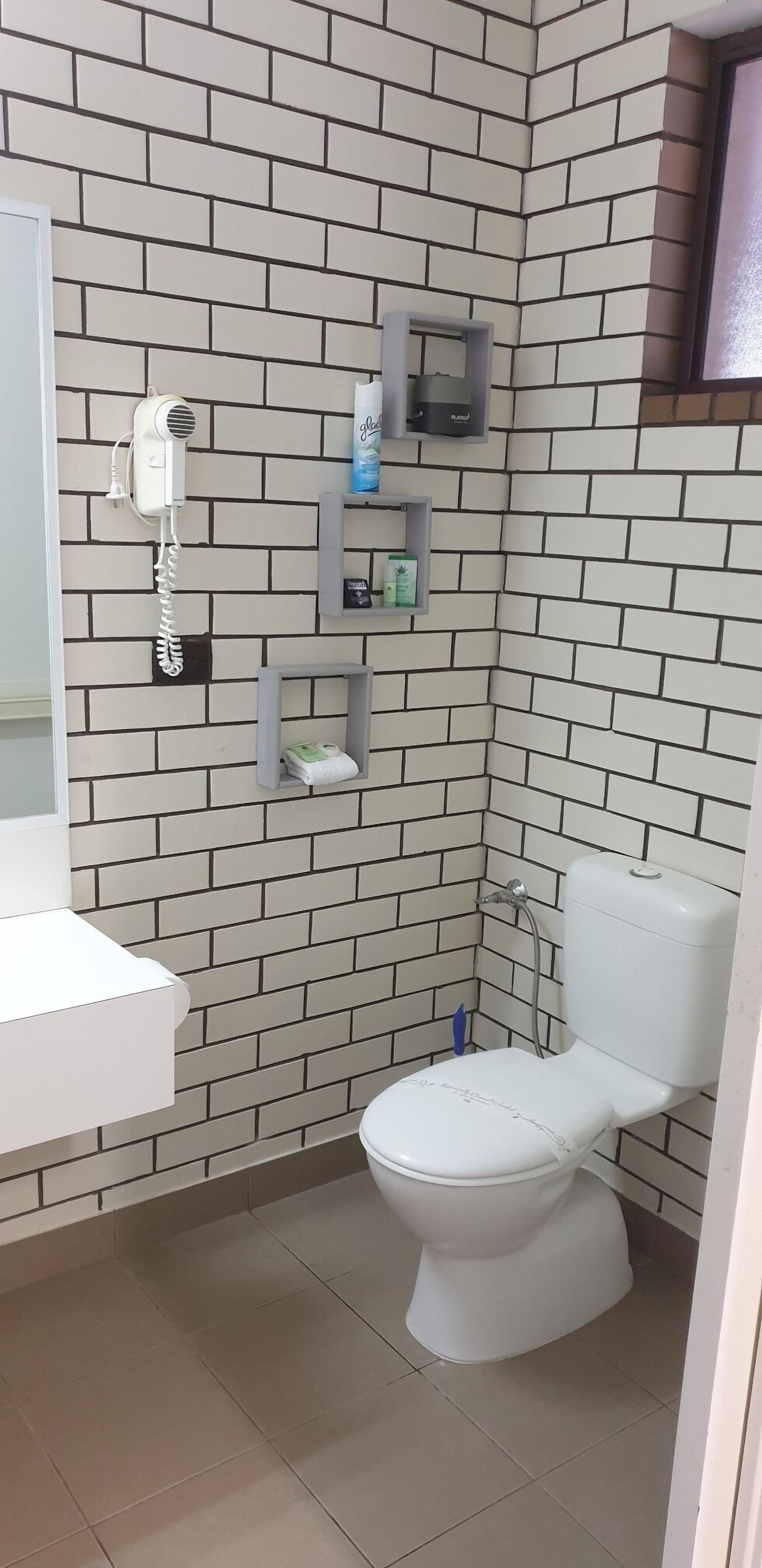 Une salle de bain avec des toilettes blanches, un sèche-cheveux et des étagères pour ranger les articles de toilette.
