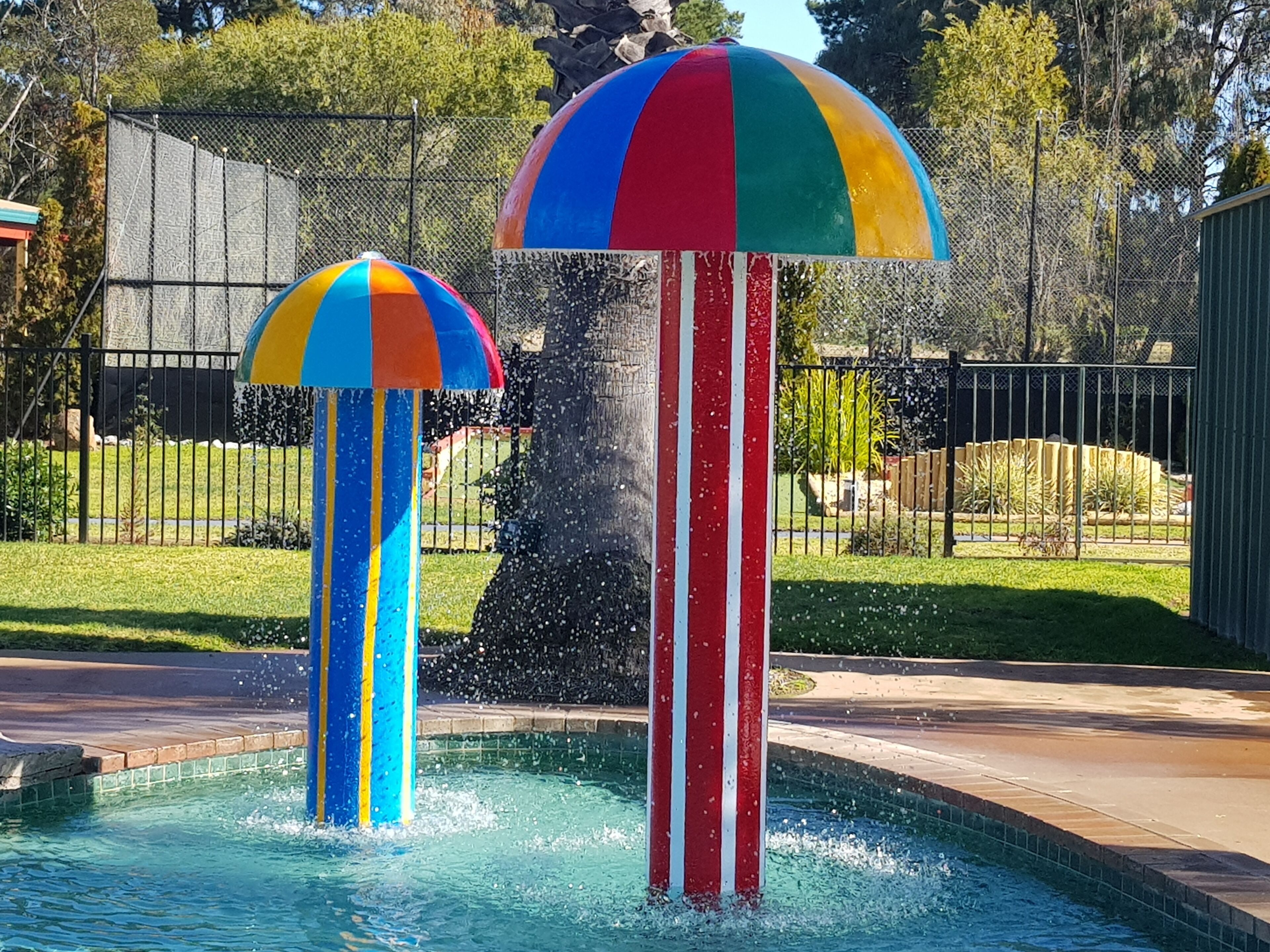 Una piscina con dos elementos acuáticos: una sombrilla colorida y un poste a rayas.