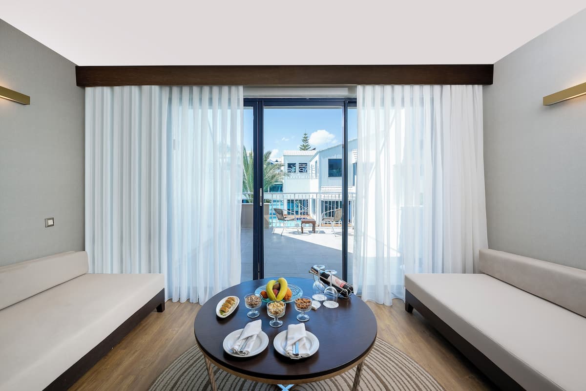 A modern hotel room with a dining table set for breakfast, a sofa, and a view of the outdoor area.