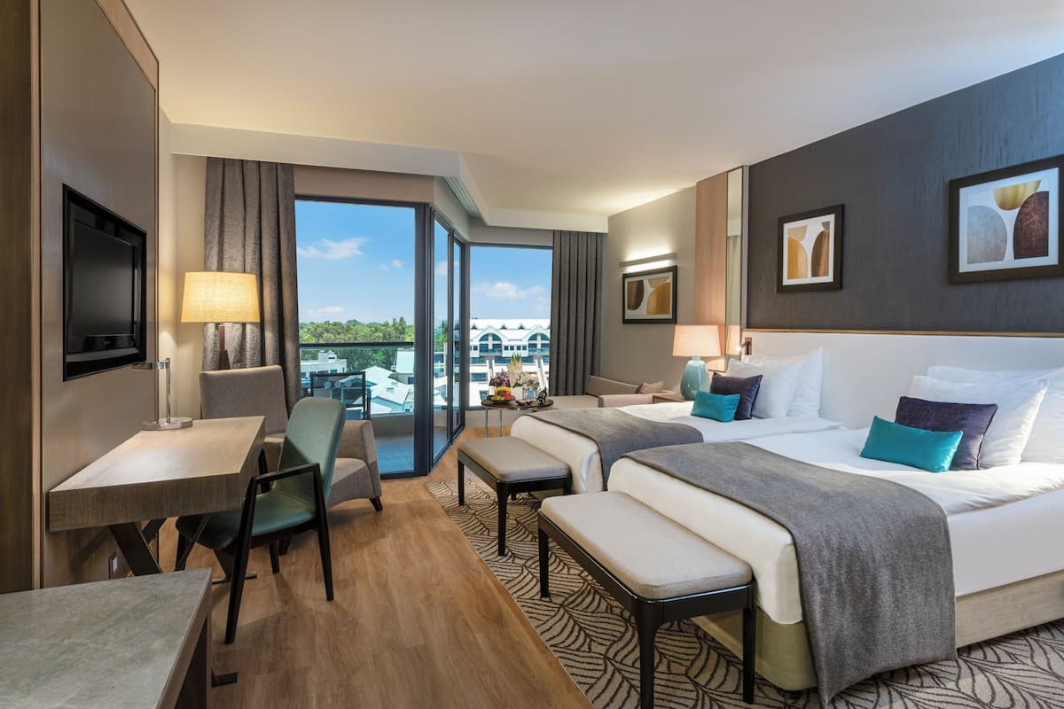 A hotel room with a bed, two bedside tables, a desk, a chair, a TV, and a balcony with a view.