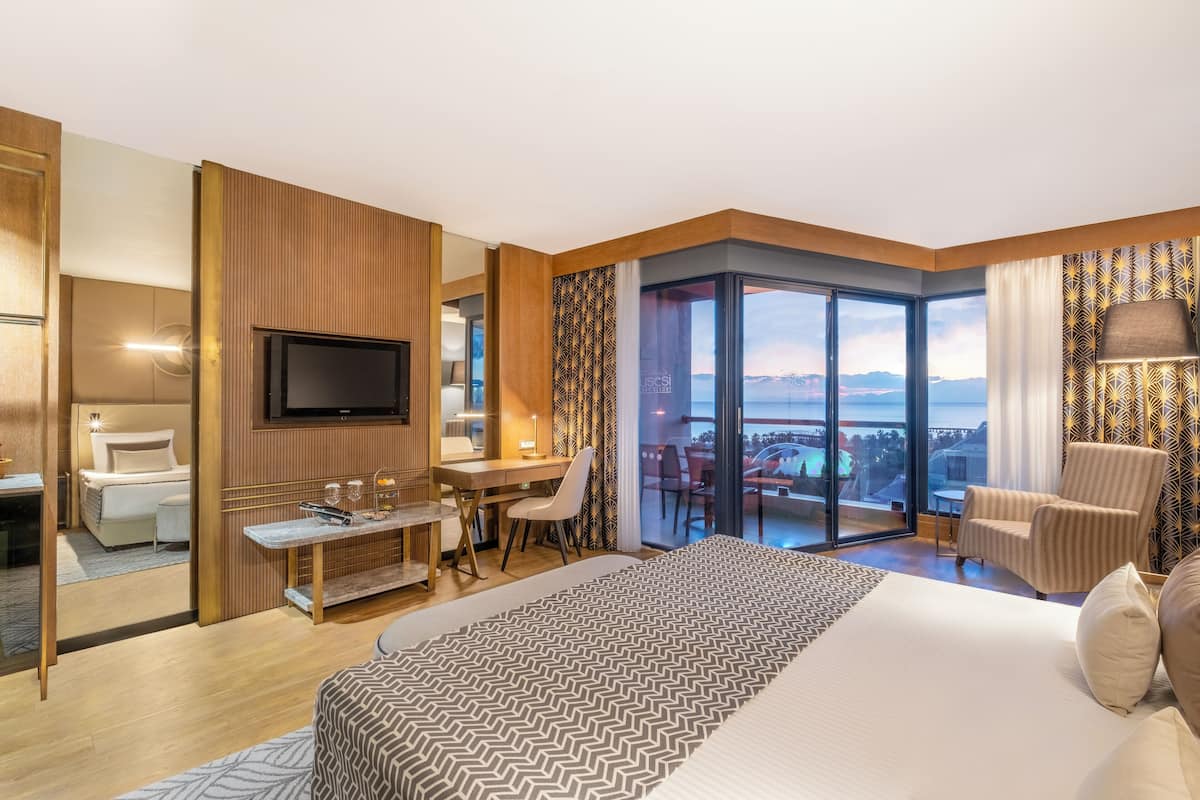 A hotel room with a bed, desk, chair, TV, and a balcony with a view.