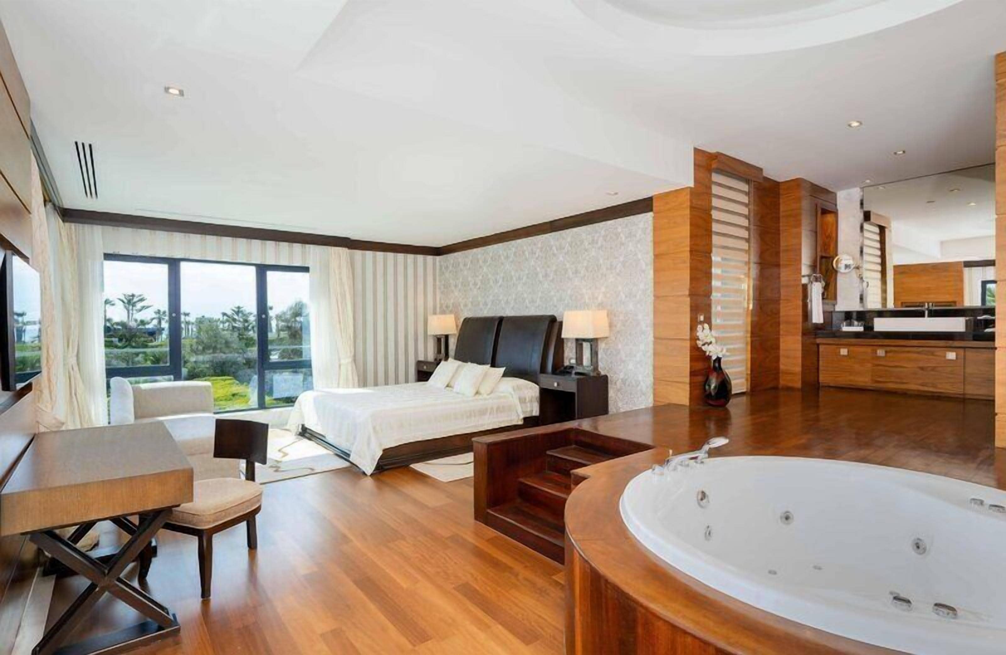 Une chambre d’hôtel moderne dotée d’un grand lit, d’un coin salon, d’une baignoire et offrant une vue sur l’extérieur.