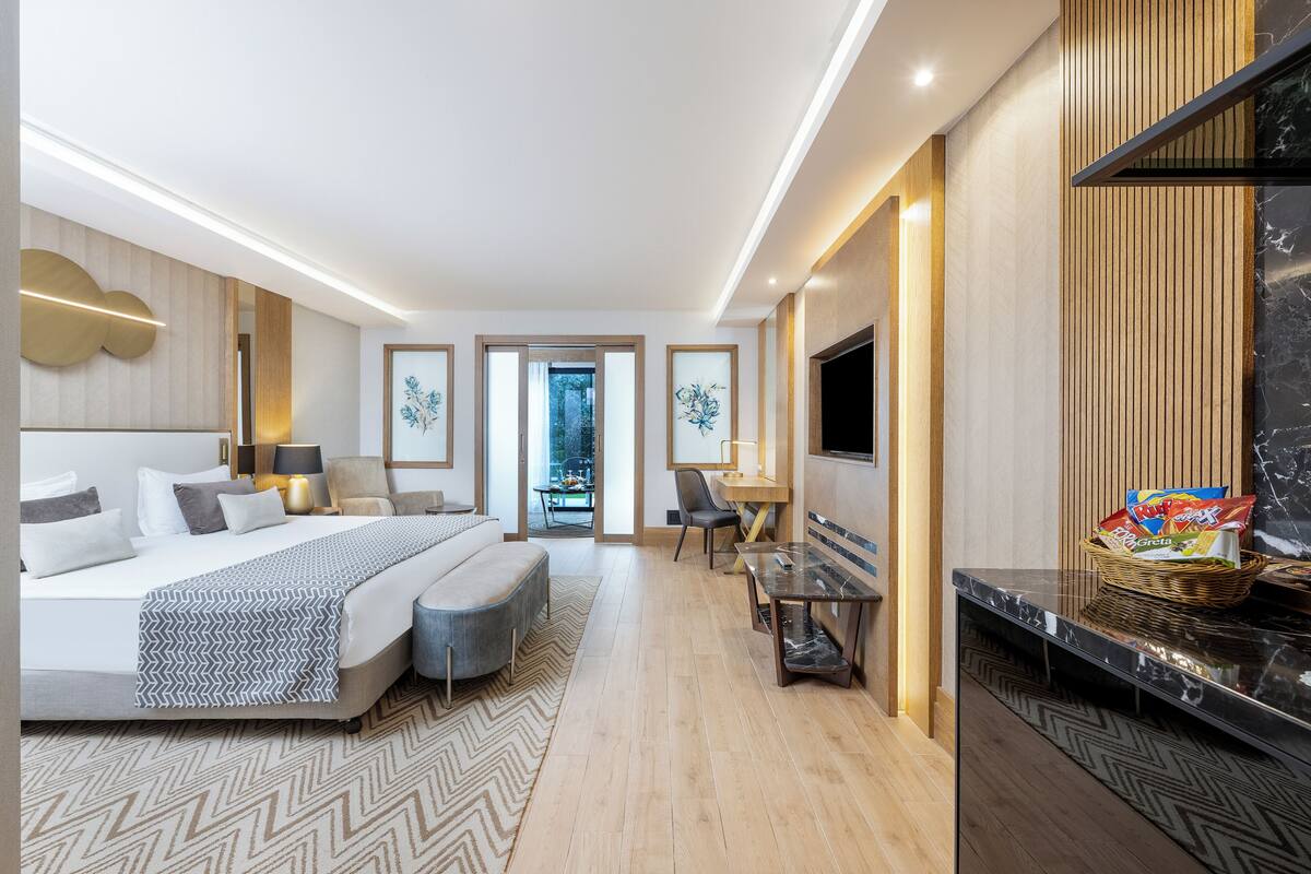 A modern hotel room with a bed, seating area, TV, and a dining table.