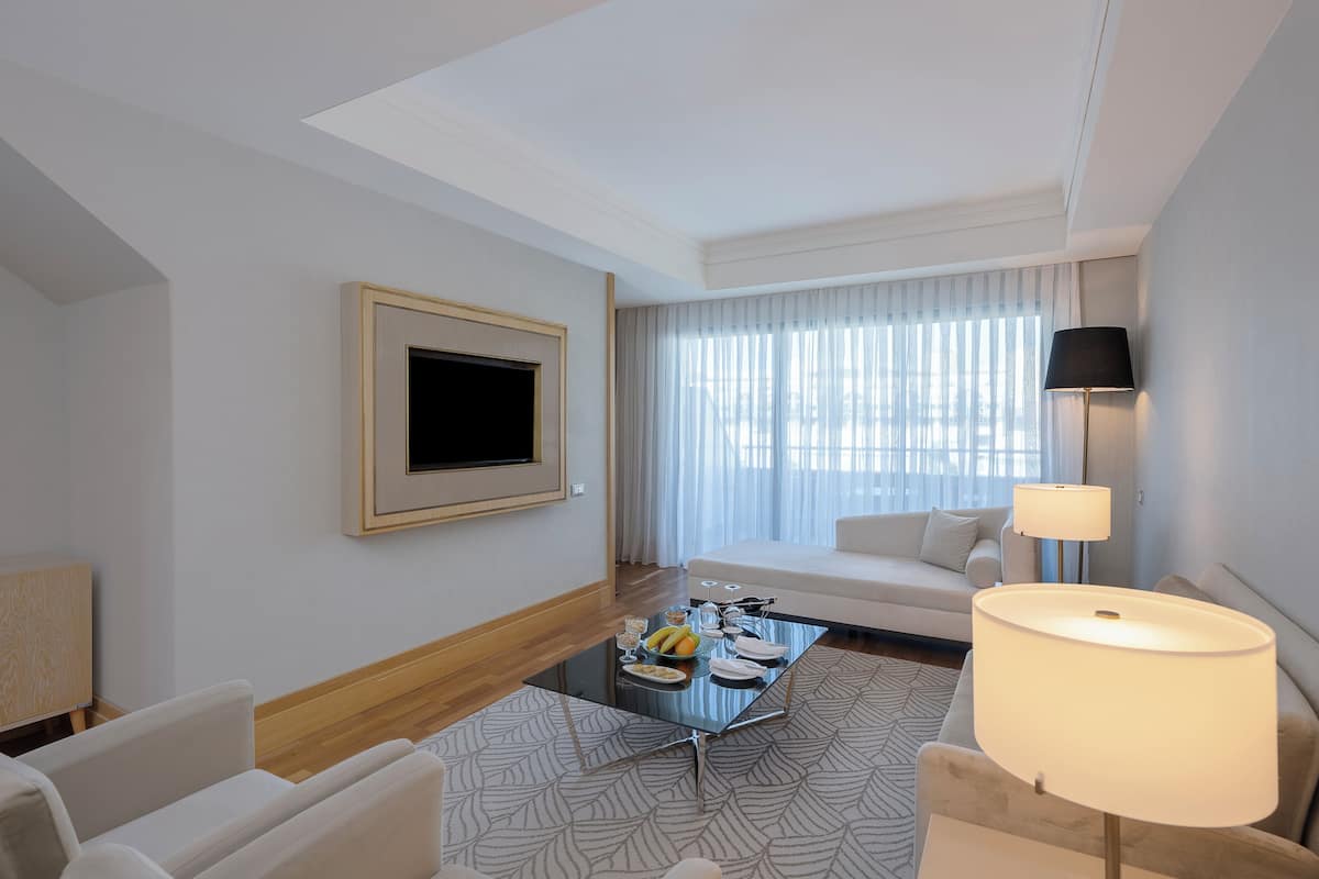 A hotel room with a sofa, a coffee table with breakfast items, a TV, and a lamp.
