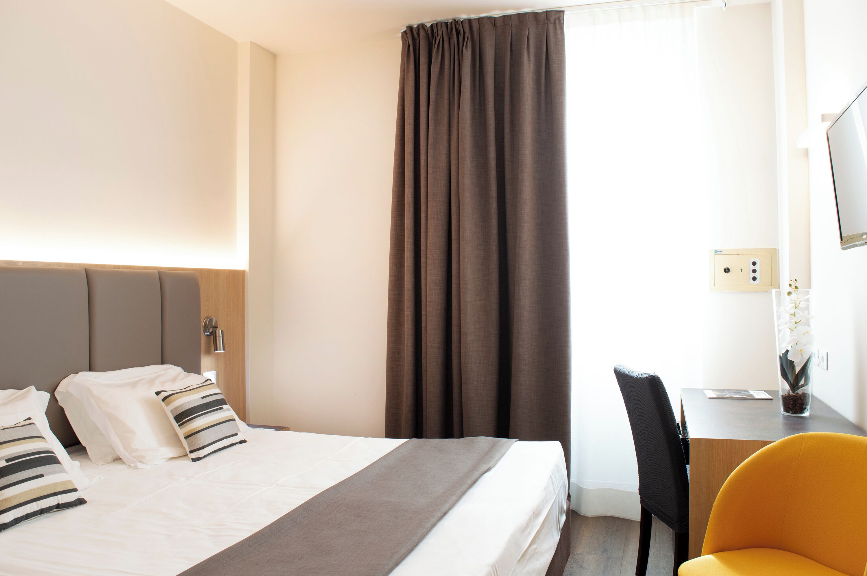 Una habitación de hotel con cama, escritorio, silla y ventana con cortinas.