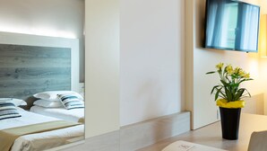 Habitación de hotel con cabecera de madera, un televisor de pantalla plana en la pared y una planta en maceta con flores amarillas sobre la mesa.