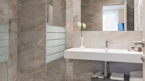 Un baño moderno con cabina de ducha de vidrio, un lavamanos blanco y un jarrón con flores.