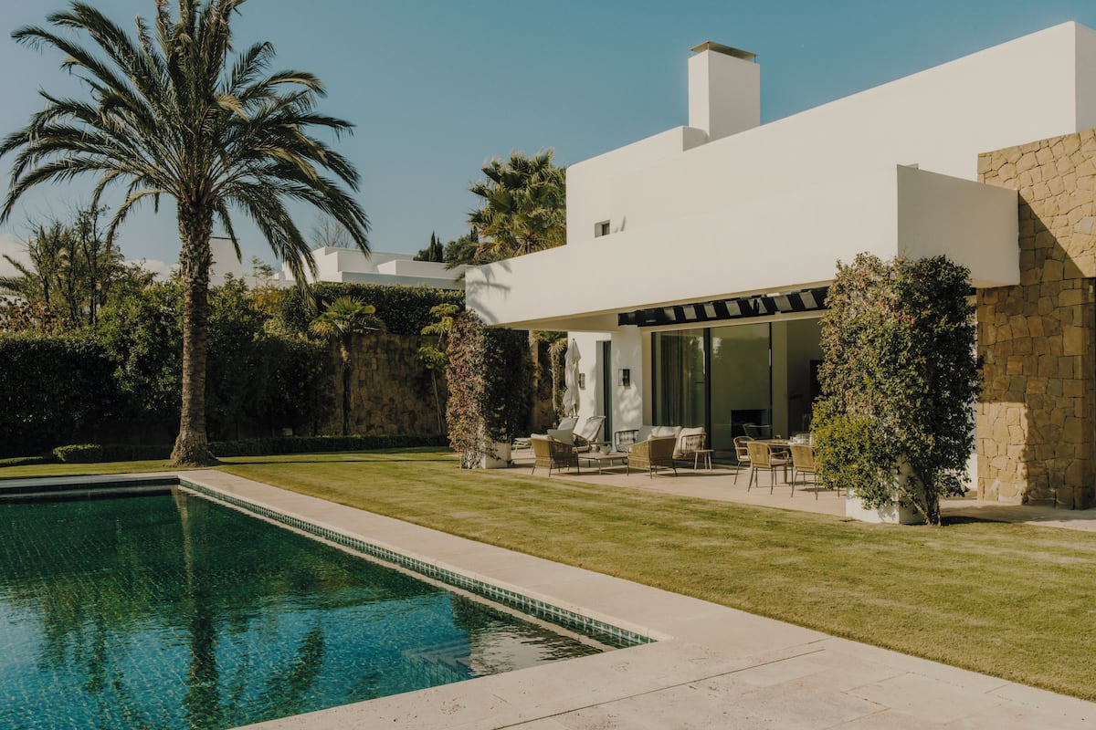 Una casa moderna con piscina, mobiliario exterior y un muro de piedra.