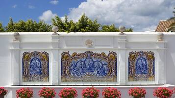 Pared blanca con azulejos decorativos azules y dorados y flores rosadas en macetas.