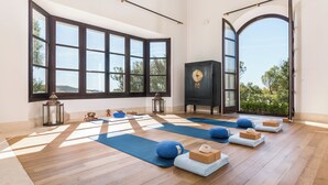 A spacious room with large windows, wooden flooring, and yoga mats arranged for practice.
