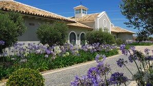 A building with a tiled roof, a small tower, and a garden with purple flowers.