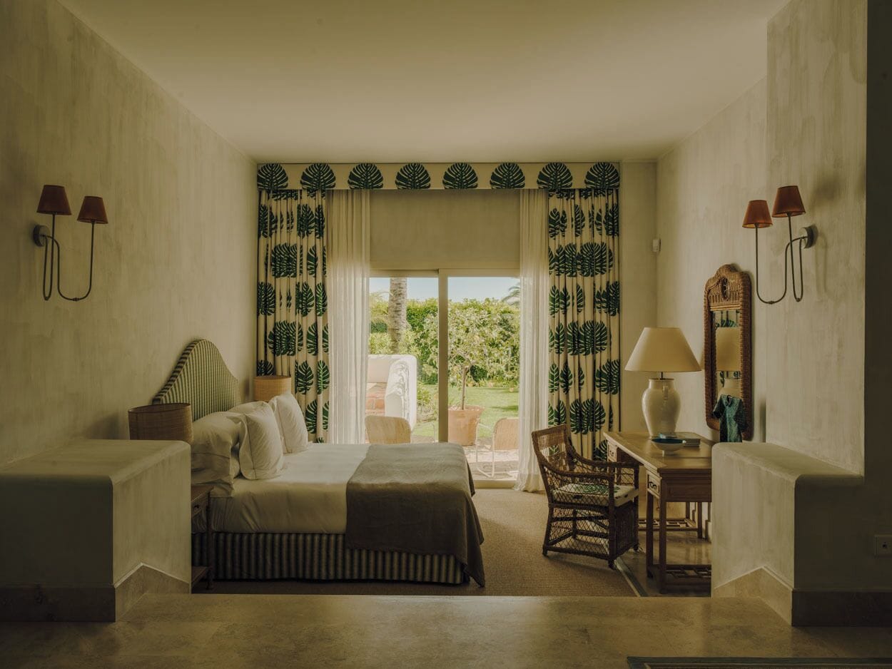 Een slaapkamer met een bed, twee nachtkastjes, een stoel, een bureau en een raam met gordijnen.