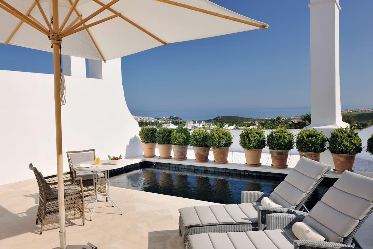 Zona junto a la piscina con sillones, una mesa y plantas en macetas.